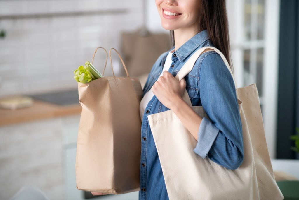 Woman with paper bag and fabric bag on his shoulder.